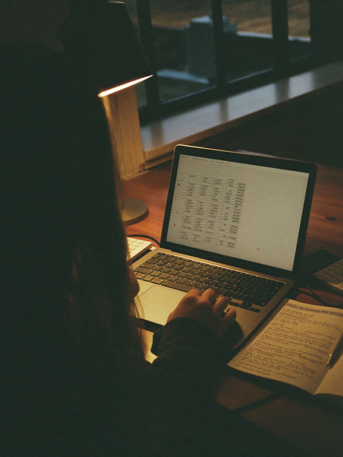 The founder at a desk in the evening, spreadsheet open, receipts at hand